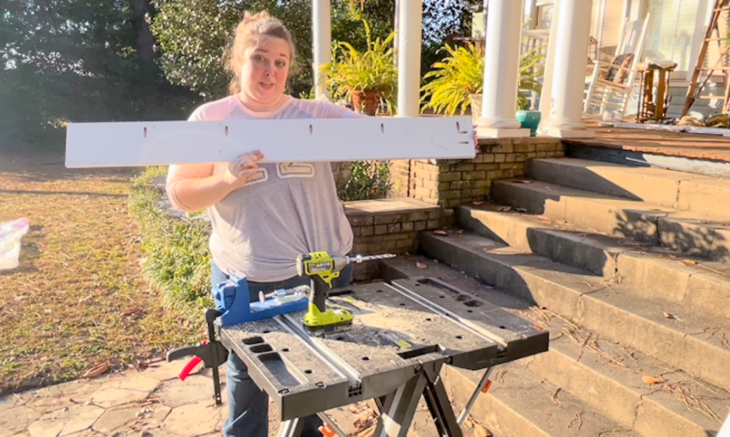 person holding piece of wood up looking at the camera, they are at a work bench person holding piece of wood up looking at the camera, they are at a work bench