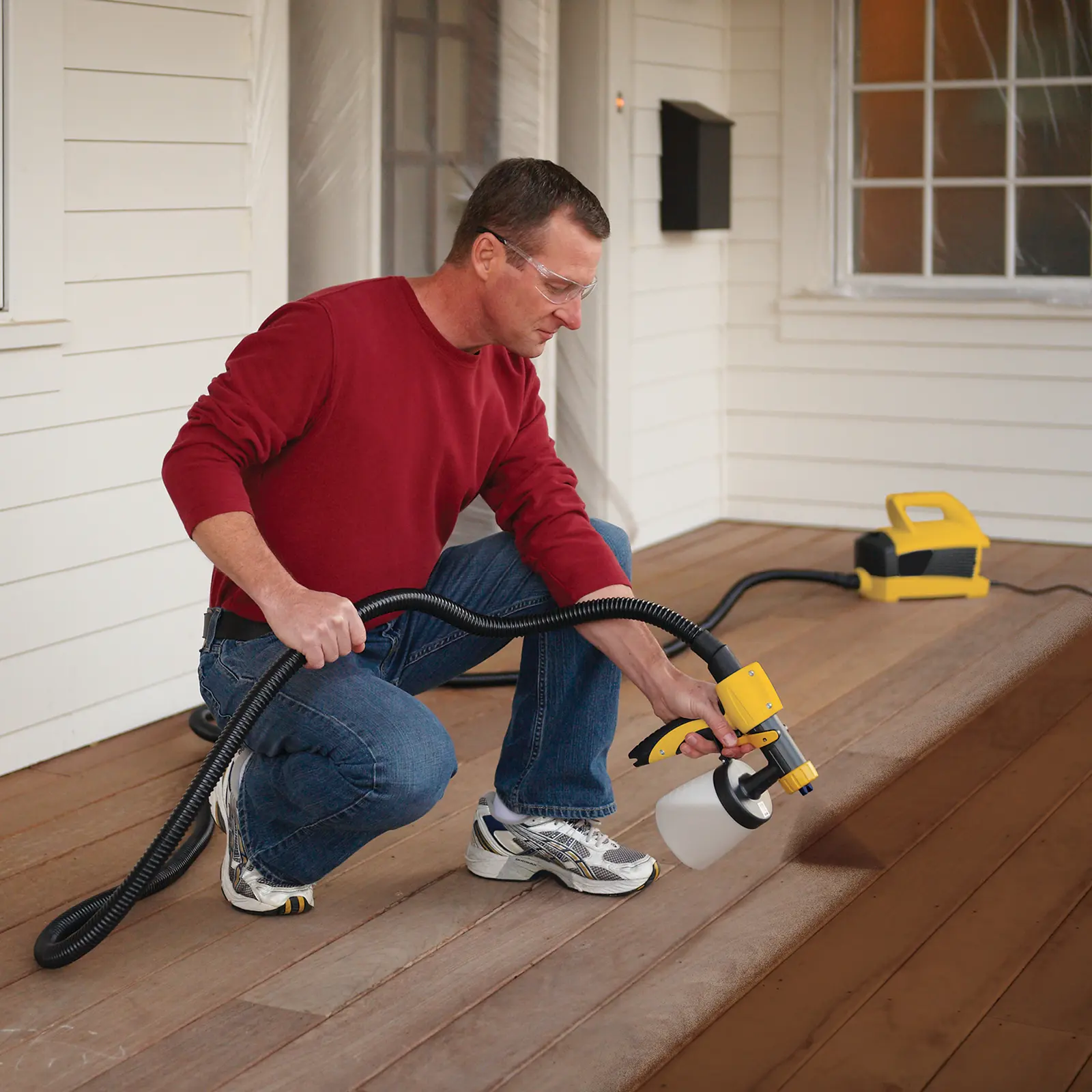 Man using a yellow power sprayer to stain a deck.