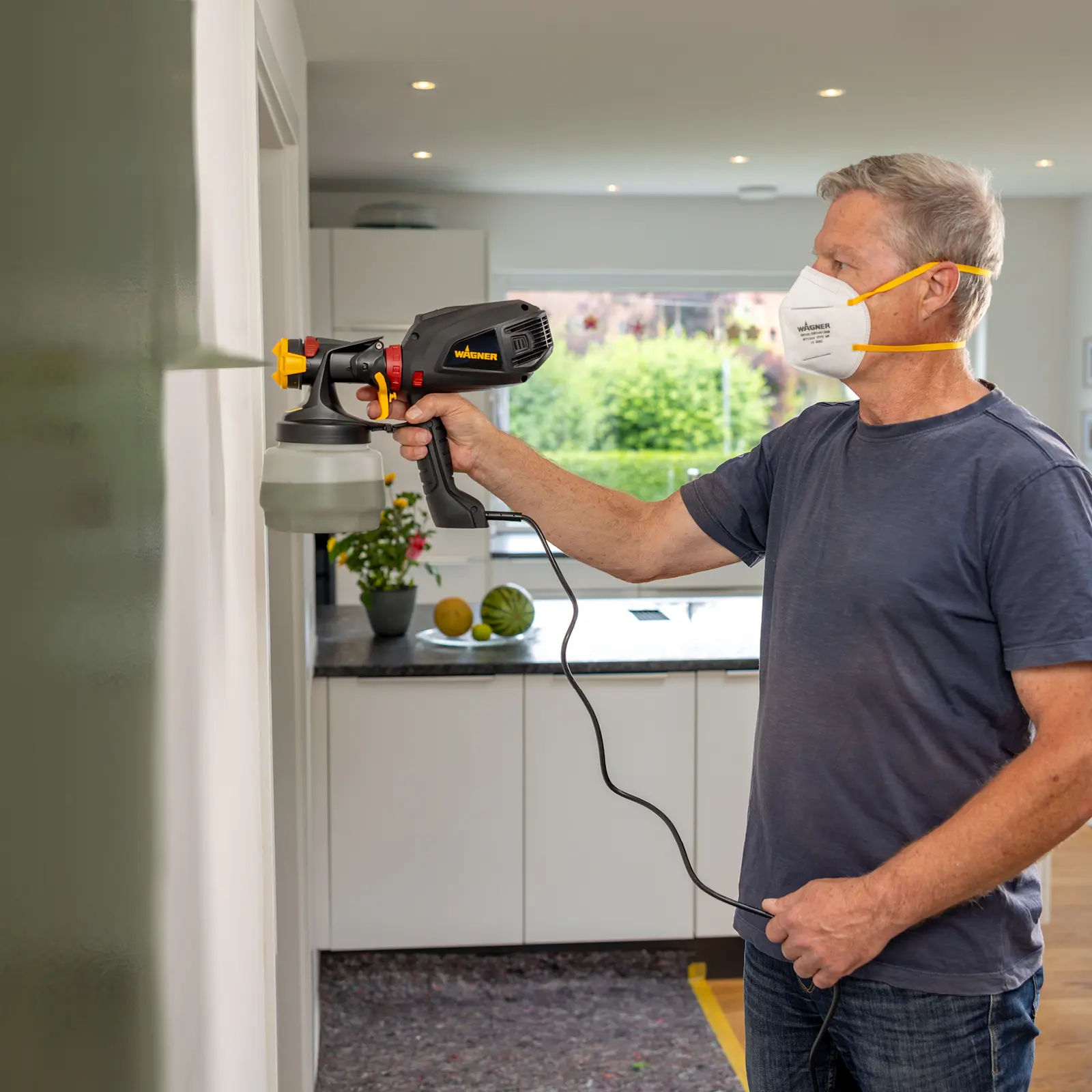Man in a mask using a Wagner paint sprayer.