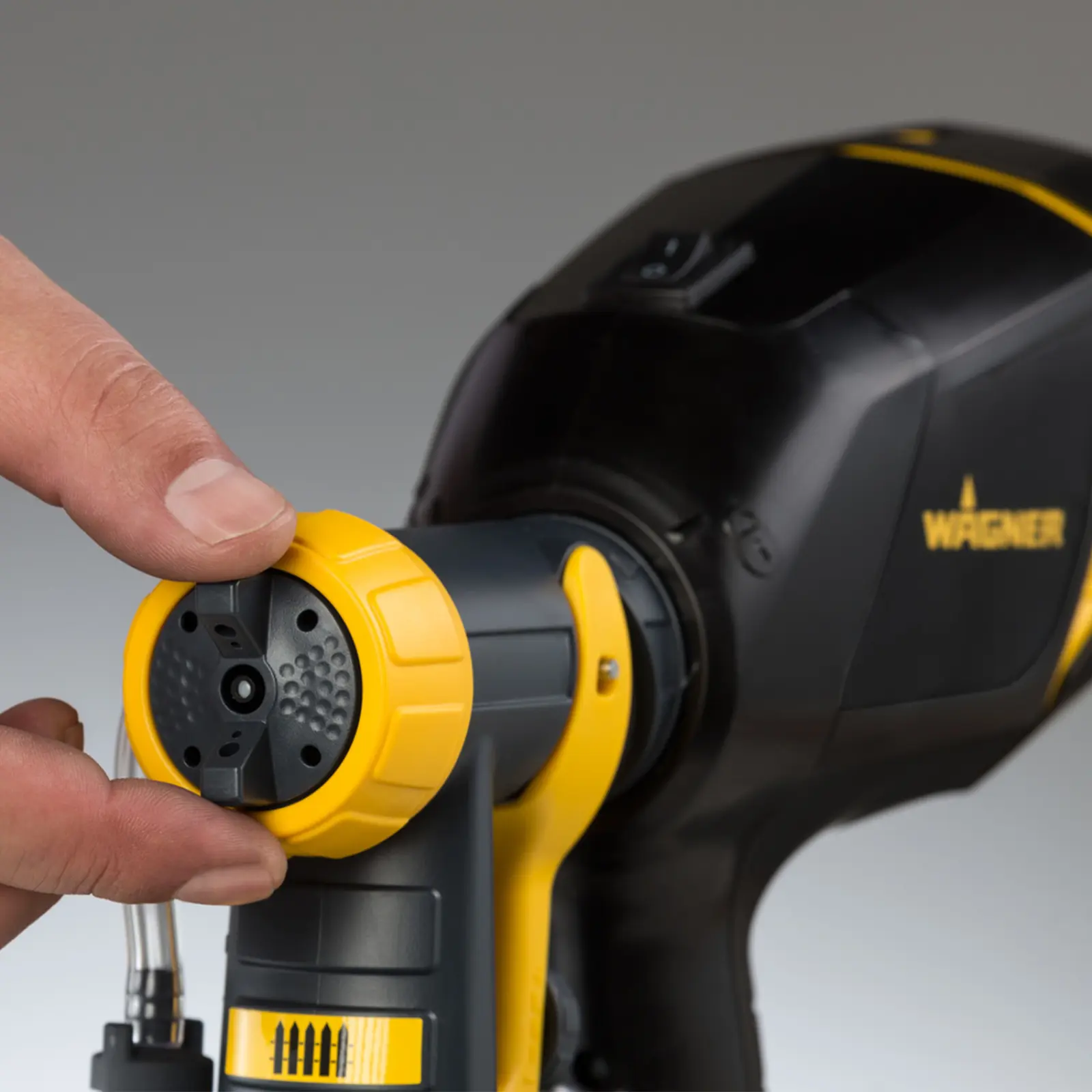Close-up of a hand adjusting a Wagner paint sprayer nozzle.