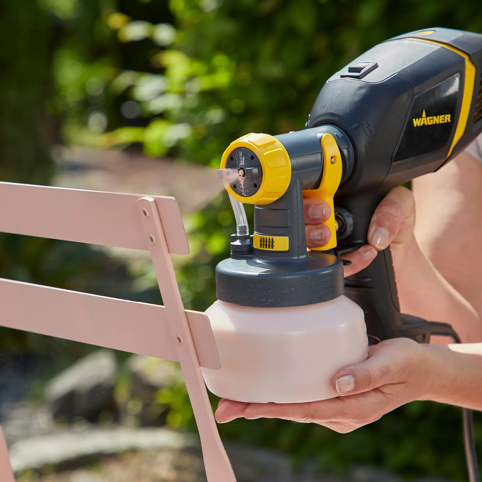 Handheld Wagner paint sprayer applying pink paint to a chair.