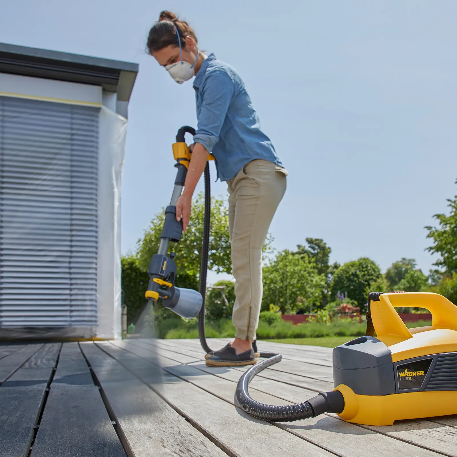 Woman staining a wooden deck with a Wagner paint sprayer.