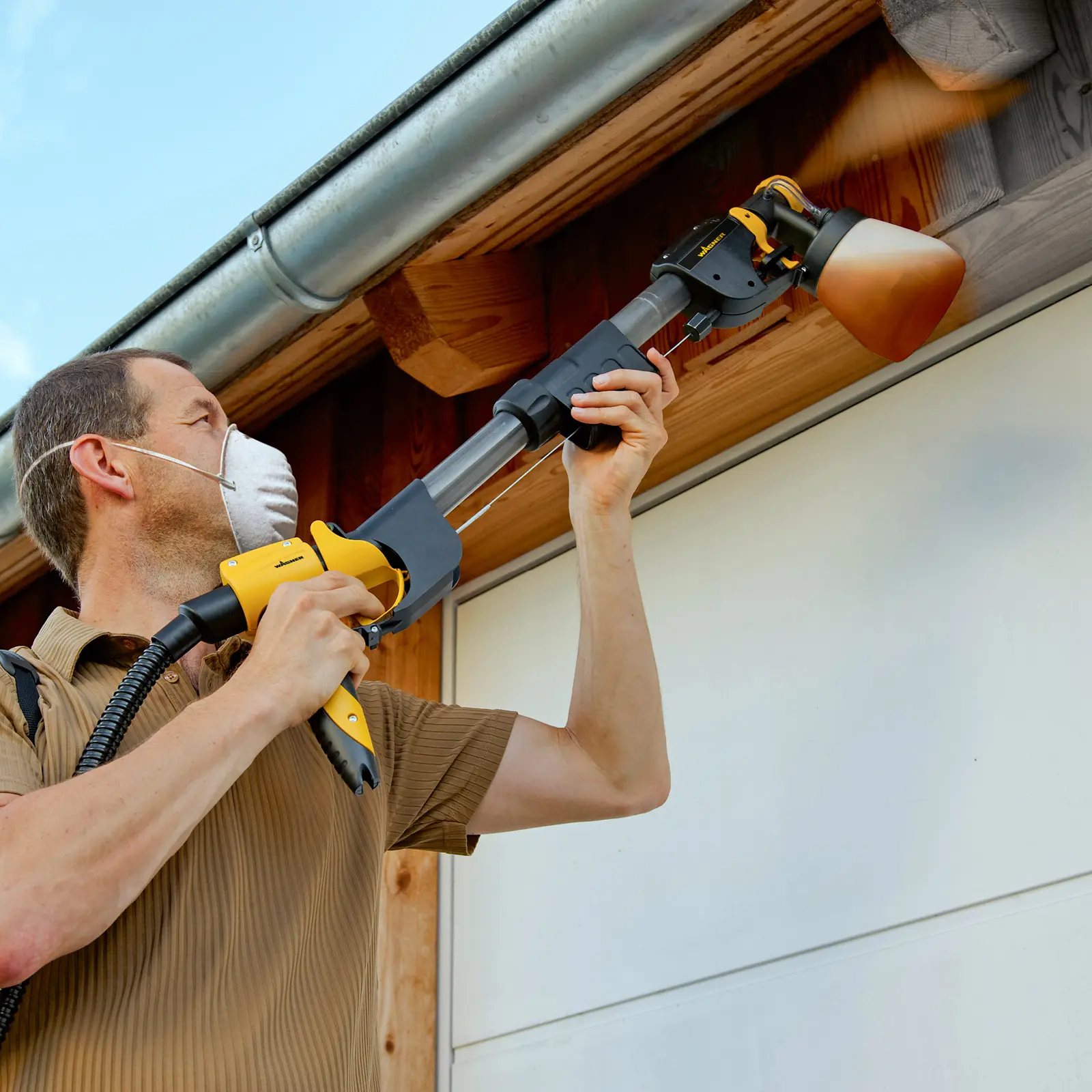 Man using a long-handled power sprayer on roof eaves.