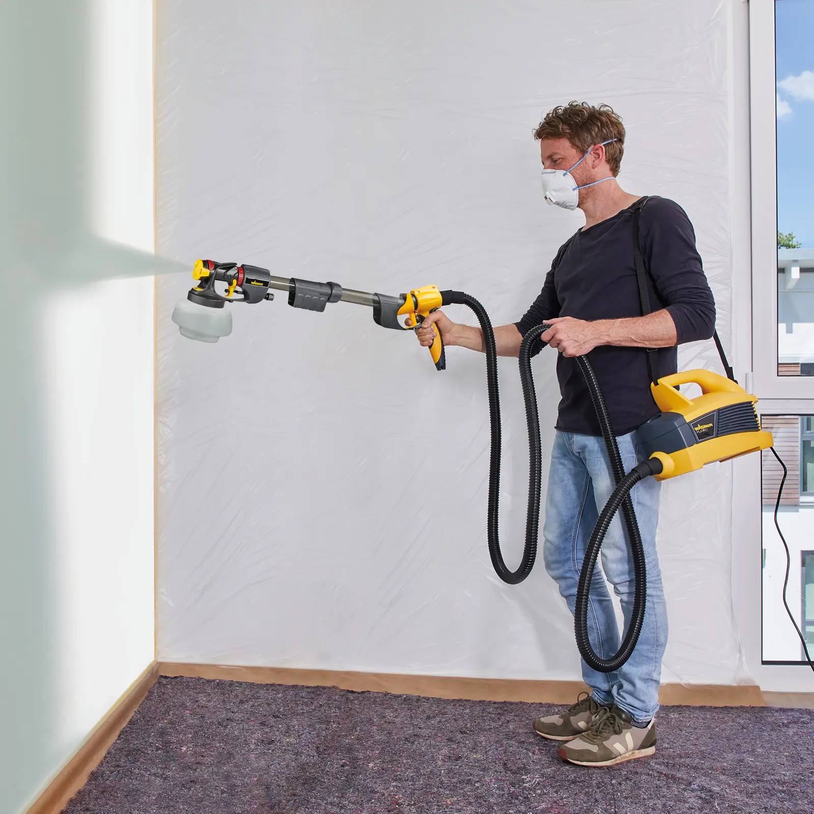 Man using a long-handle paint sprayer on a wall.