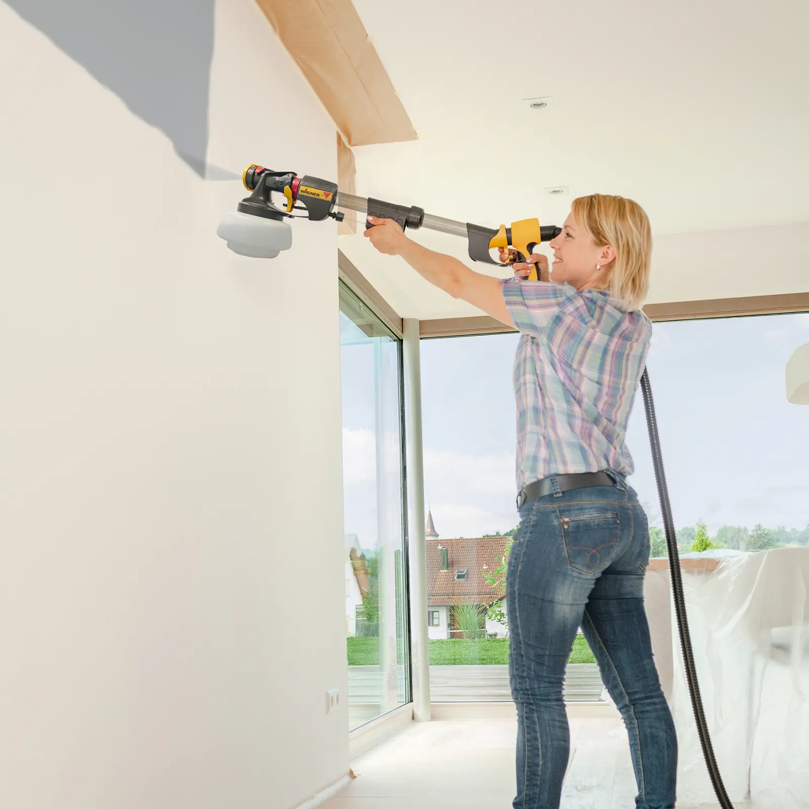 Woman painting high walls with a long-handled paint sprayer.