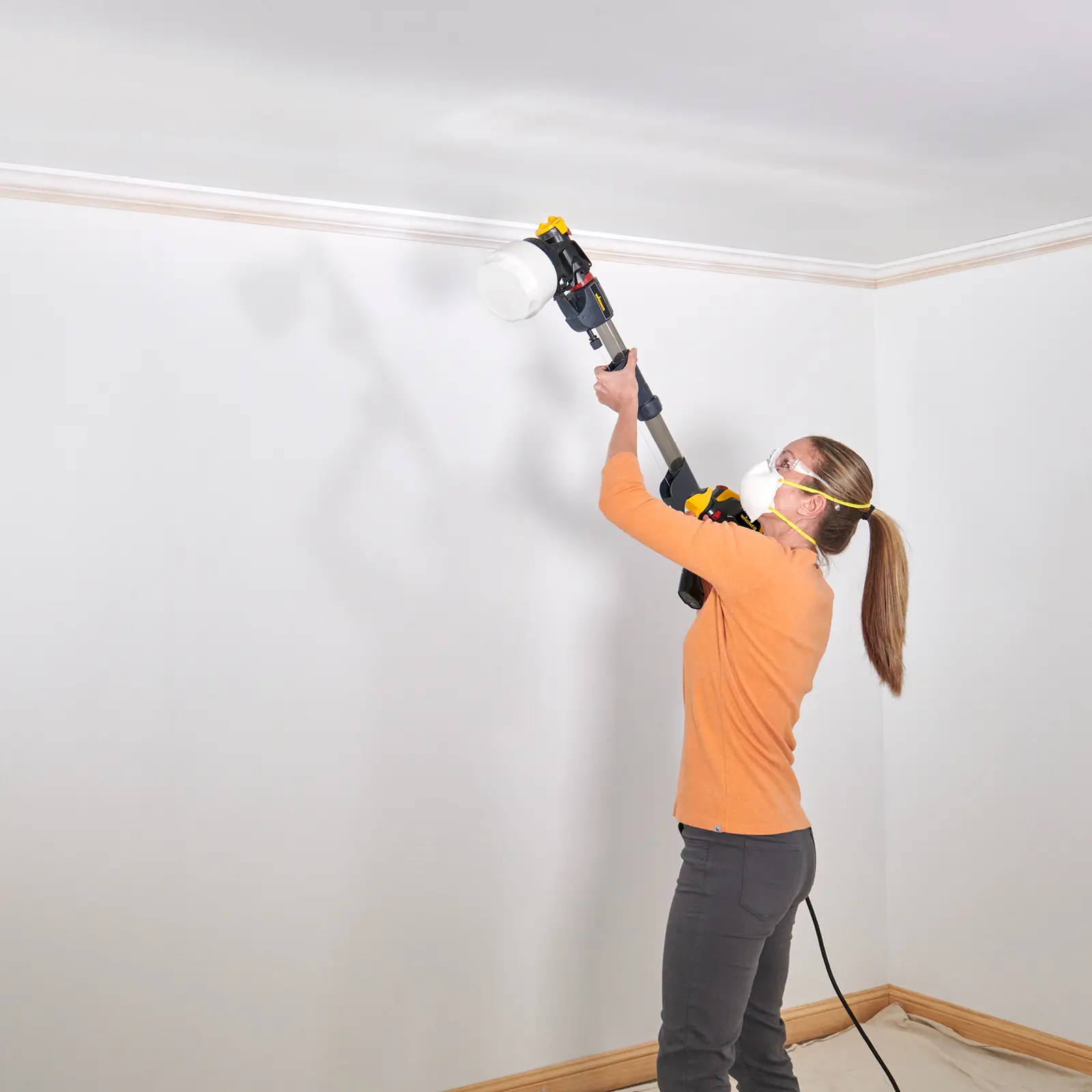Woman using a long-reach power paint sprayer on ceiling.