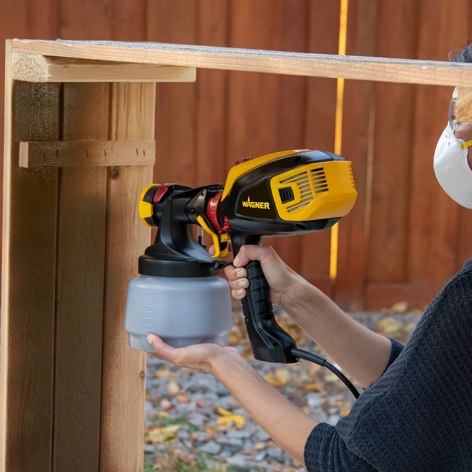 Person using a yellow Wagner paint sprayer on wood.