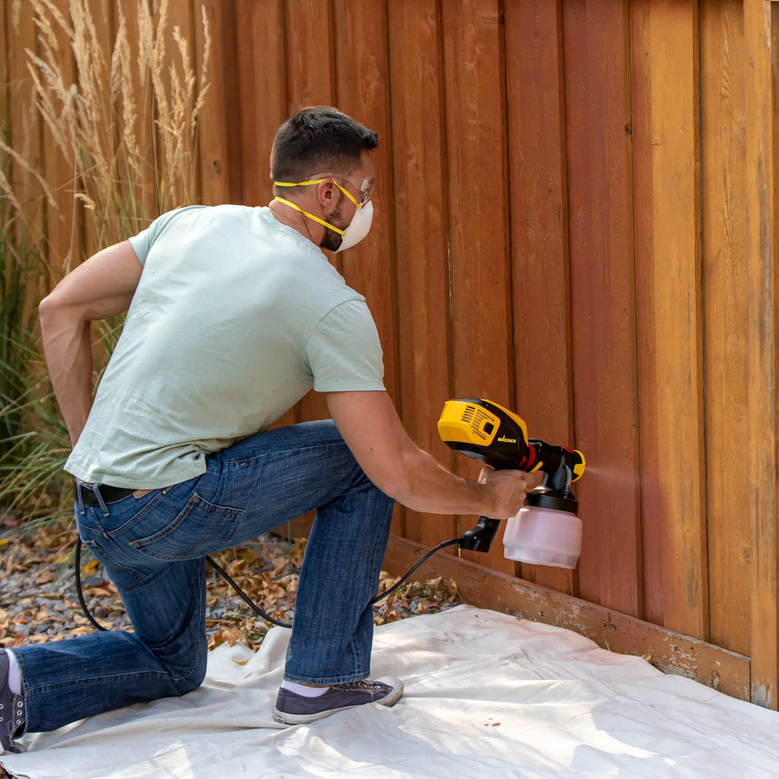 Man using a power sprayer to stain a wooden fence.