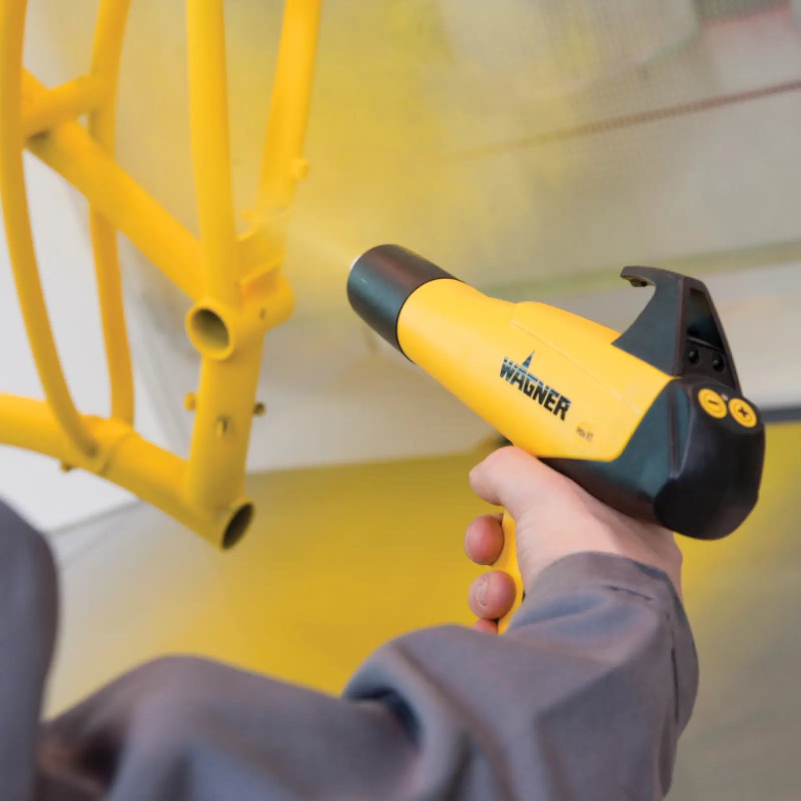 Hand applying yellow powder coat to metal frame with Wagner gun.