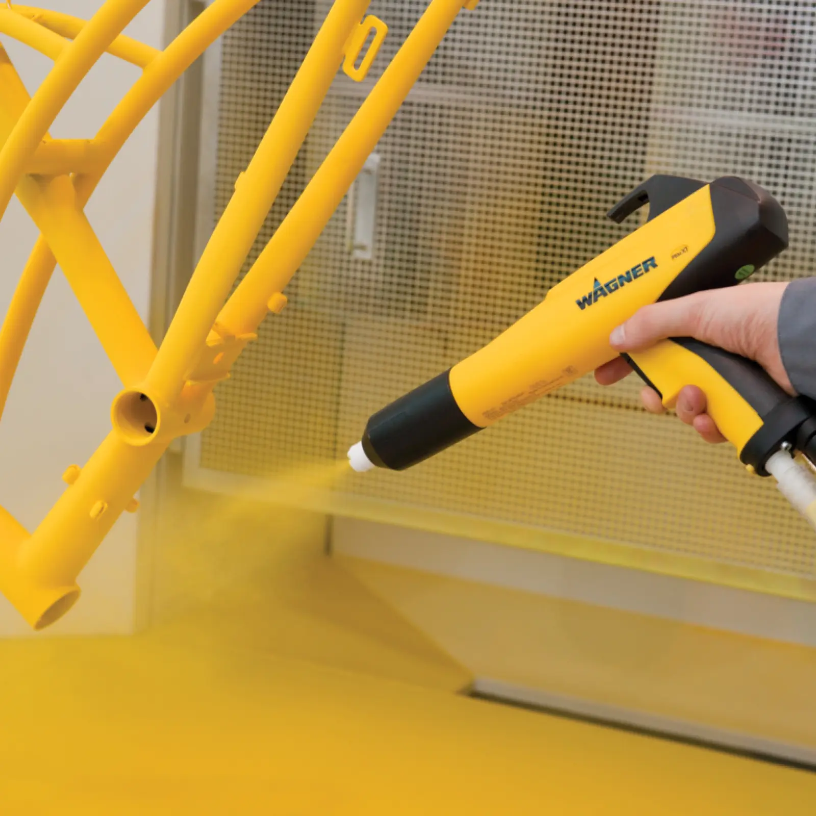 Hand powder coating yellow metal frame with Wagner spray gun.