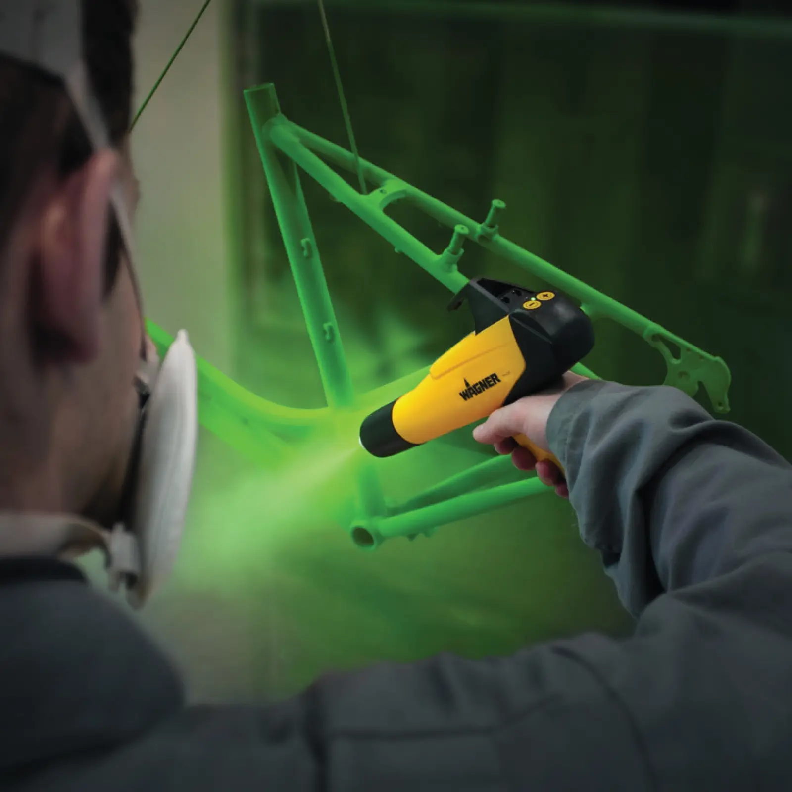 Person powder coating a green bicycle frame with a Wagner gun.