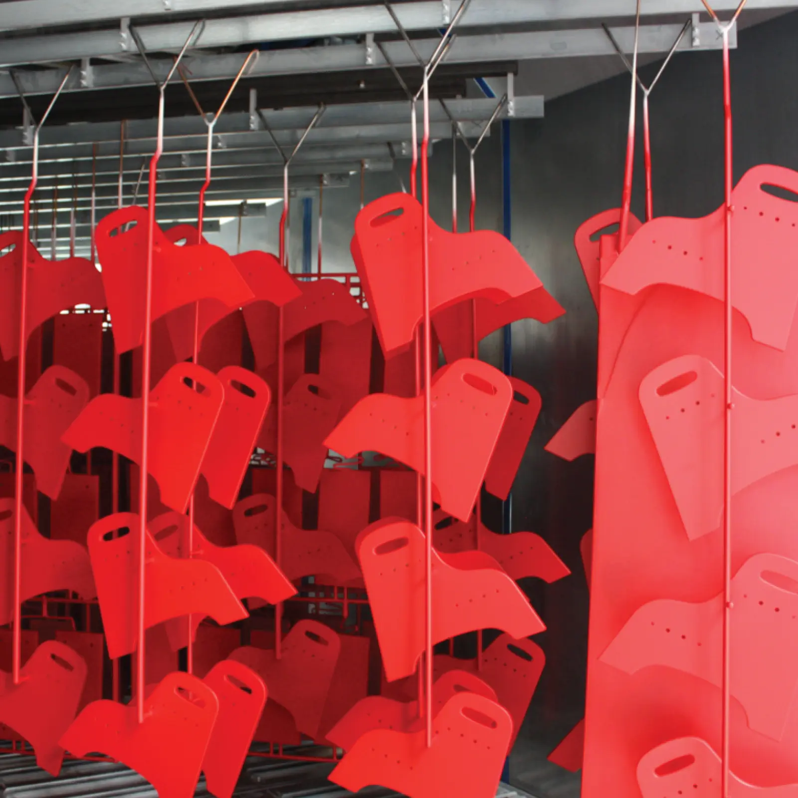 Red metal parts hanging on conveyor in industrial finishing process.