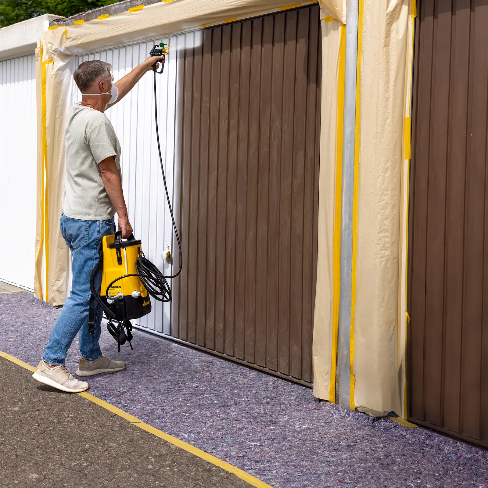 Man spray painting garage door white with a paint sprayer.