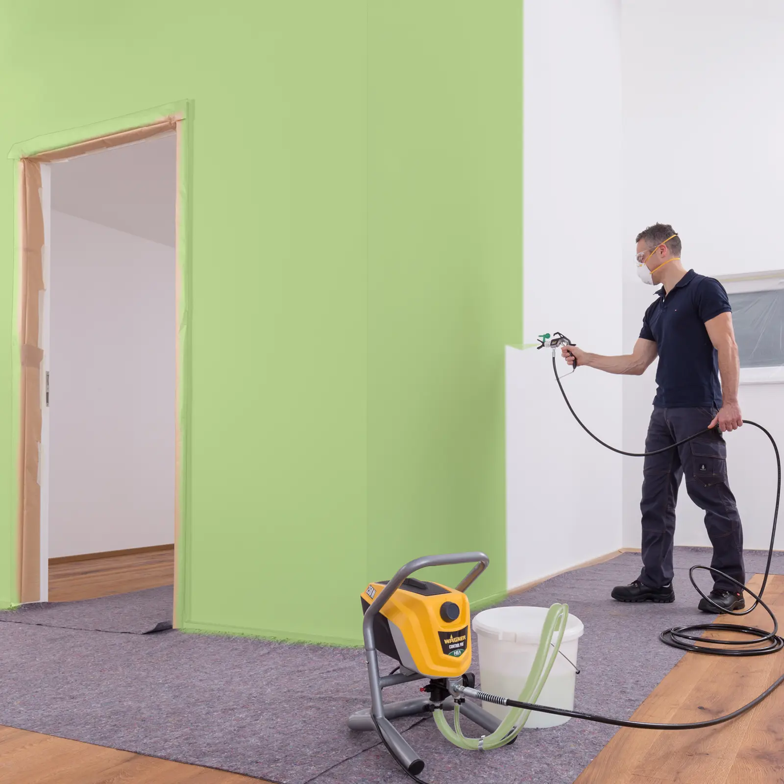 Worker spray paints interior wall bright green with professional equipment.
